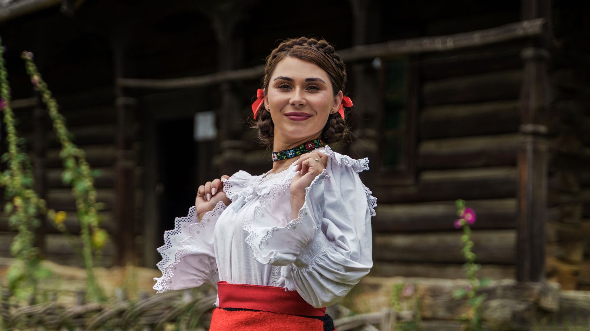 Andreea Ghițiu în costum tradițional, în fața unei case din lemn
